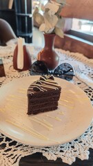 Slice of rich chocolate cake with white drizzle on a ceramic plate in a cozy vintage cafe. Concept of indulgence, comfort and the charm of rustic elegance