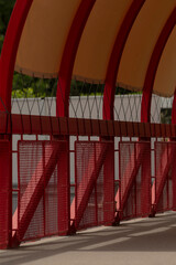 This image shows a closeup of a vibrant red architectural structure with a curved overhead design and strong metal framework, showcasing modern engineering and creativity