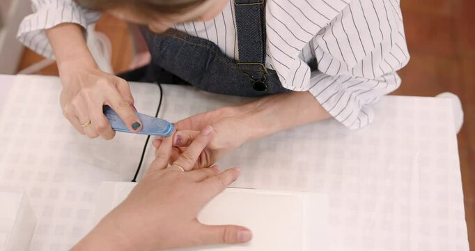 asian female manicurist using blue buffer tool to shape fingernails for senior asian woman during manicure step inside small local nail salon demonstrating careful and professional handcare work