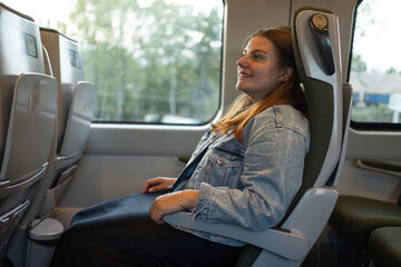 A smiling woman sits by the window in a modern Polish train, enjoying her journey. A warm and...