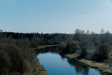 Summer dayscape with river or lake around green forest and fields