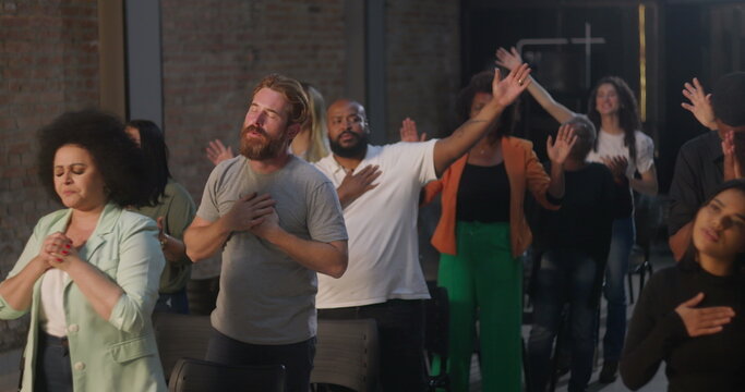 Congregation standing in prayer, hands on hearts, diverse group in worship, spiritual connection and devotion, indoor church setting with emotional reflection and unity
