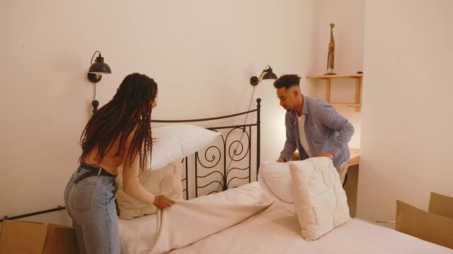 A man and woman are putting pillows on the bed while making it