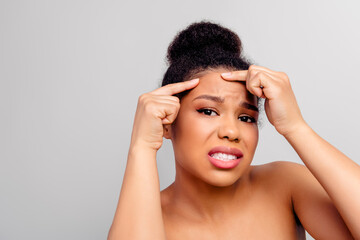 Young woman expressing concern while examining her skin in a clean setting, depicting skincare and...