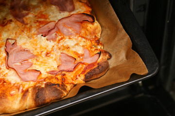 Fresh homemade pizza baking. Crispy crust and melted cheese. Hot oven tray with ham topping....