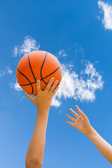 Hands Reaching for a Basketball Under a Blue Sky