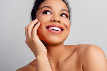 Smiling young woman with natural makeup and radiant skin posing on a plain background, expressing...