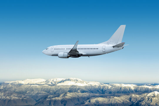 Fototapeta White modern jet plane flies over snow covered mountains