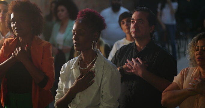 Congregation worshipping with hands on heart during evangelical church gathering, African descent preacher delivering inspiring message, spiritual unity and devotion