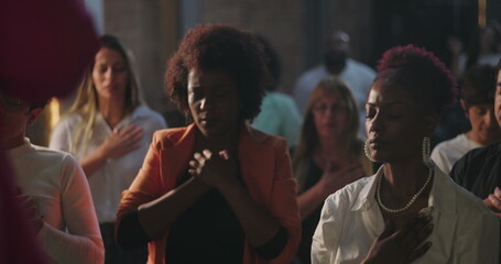 Fototapeta premium Diverse group of Christian worshippers in prayer, hands on hearts, eyes closed, deep spiritual connection in evangelical congregation