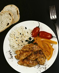 Roasted chicken breast dinner with rice, colorful bell pepper, and fresh tomato, served on a plate for healthy meal.
