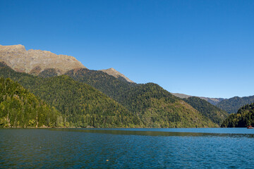 Lake Ritsa surrounded by mountain peaks. Boats sail on smooth turquoise water.  Sunny autumn day