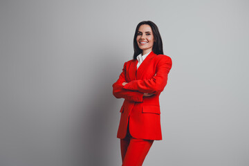 Confident businesswoman in red suit posing with arms crossed against a neutral background, exuding professionalism