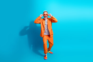 Charismatic mature man in vibrant orange suit and playful glasses against a bright blue background showcasing style and joy