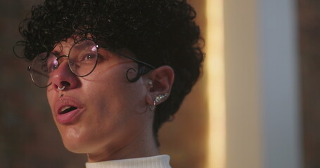 Woman with curly hair, wearing glasses, reflecting deeply with teary eyes during emotional moment...