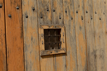 A rustic wooden wall has a square opening secured by a durable metal grate, enhancing both the aesthetic appeal and safety, adding character and fortification to the design