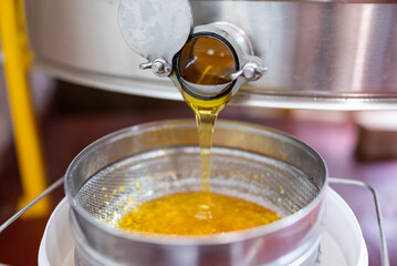 Fresh honey flows from extractor into bucket through filter. Collected honey drips from stainless...
