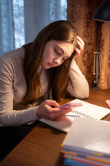 Tired teen girl taking a break from study with phone. Teenage girl pausing from schoolwork, holding...