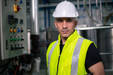 An industrial engineer wearing a safety helmet and reflective vest stands confidently in front of a...