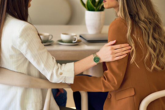 Two women, business colleague sitting in armchairs and talking while having coffee . Woman psychologist talking to patient. Close-up image of supporting hands of friend.