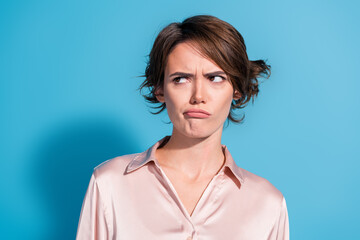Young woman with expressive face against blue background in satin shirt, expressing doubt and...