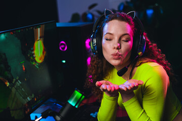 Young female gamer streaming live, wearing a gaming headset, and engaging with her audience in a...