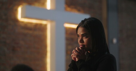 Hispanic woman looking upward in prayer, hands clasped in deep reflection and connection to faith...