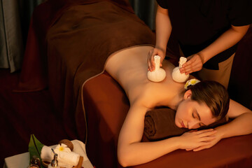 Hot herbal ball spa massage body treatment, masseur gently compresses herb bag on woman body....