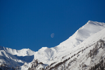 Landscape of a moon above the snowy mountains of the Alps in the daytime in spring © Titas