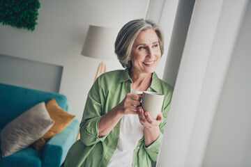 Relaxed senior woman enjoying coffee indoors with a bright smile in comfortable home setting during...