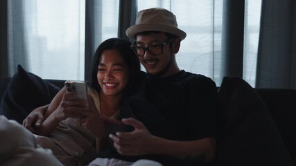 Happy young Asian couple using smartphones while relaxing and watching series together - Powered by Adobe