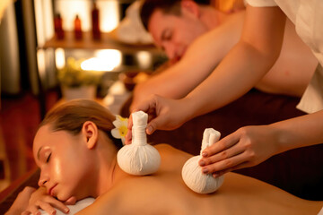 Hot herbal ball spa massage body treatment, masseur gently compresses herb bag on couple customer...