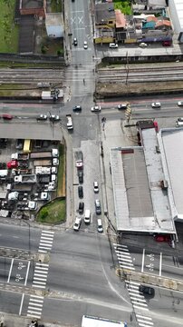 Vis&atilde;o a&eacute;rea vertical de ve&iacute;culos em um cruzamento com farol de tr&acirc;nsito. A imagem mostra carros parados e em movimento, ilustrando o controle do tr&aacute;fego urbano em uma cidade movimentada