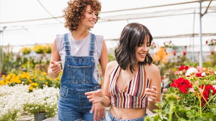 Fototapeta premium Two female garden center workers walking and smiling among flowers