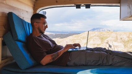 Freelancer working remotely on laptop in camper van enjoying mountain view in gorafe, spain
