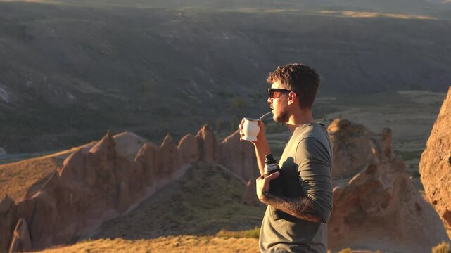 Caucasian man with sunglasses drinking mate from in Los Bolillos rock formations at the background. Neuquen, Argentina