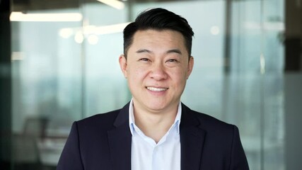 Portrait of smiling asian businessman in formal suit standing at workplace in modern business office. Head shot confident happy successful entrepreneur manager looking at camera in workspace. Close up - Powered by Adobe
