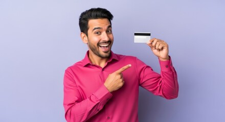 Happy man holding credit card against purple background demonstrating online shopping concept