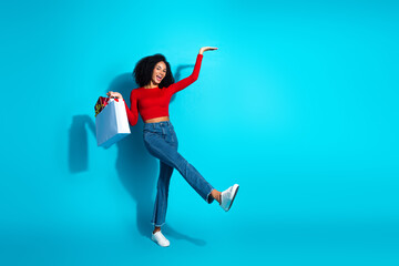 Joyful young woman with shopping bag poses in vibrant outfit against blue background