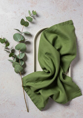 Textured green linen cloth with eucalyptus branch on ceramic tray, minimalist composition, natural vibe
