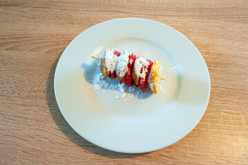 Plate with traditional dutch batter cakes and strawberry slices on a stick, sprinkled with powdered sugar