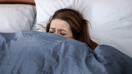Mental health concept. Depressed young woman hiding under blanket on bed, suffering from depression, stress or insomnia. Unhappy lady feeling desperate or lonely, having psychological problem