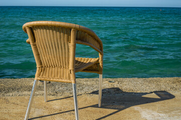 a single wicker chair sits on a concrete pier overlooking the calm, clear turquoise ocean on a sunny day with a bright blue sky concept of relaxation and coastal tranquility