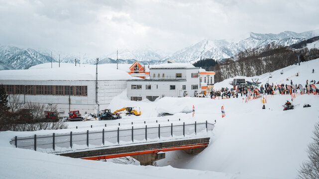 Crowds gather at Gala Yuzawa ski resort in Japan, surrounded by snow-covered mountains and pine forests. Visitors prepare for skiing and snowboarding amid scenic alpine views and winter excitement.