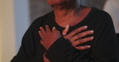 An elderly African American woman with her hands pressed to her chest in a moment of emotional...