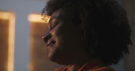 Close-up of woman with curly hair smiling, deeply engaged in prayer in front of illuminated cross...