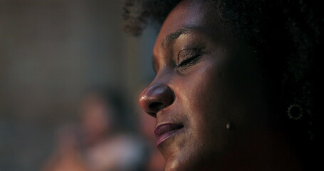 Close-up of woman with curly hair, emotionally moved during spiritual moment in church, illuminated...
