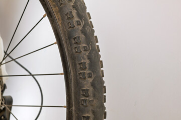 A detailed close-up of a worn bicycle tire with remaining side studs, showing a black rim, metal spokes, and part of the rear gear mechanism