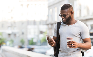 On my way to work. Cheerful bearded african man using his smartphone and drinking coffee, panorama, free space