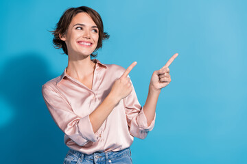 Charming young woman in satin pink blouse exuding elegance on a blue background, pointing gestures...
